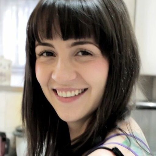 Smiling woman with dark hair and bangs in a bright room.